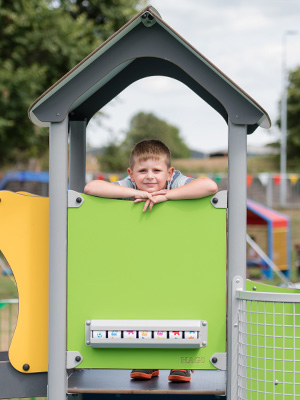 A young boy looks through a playhouse window at a playground.